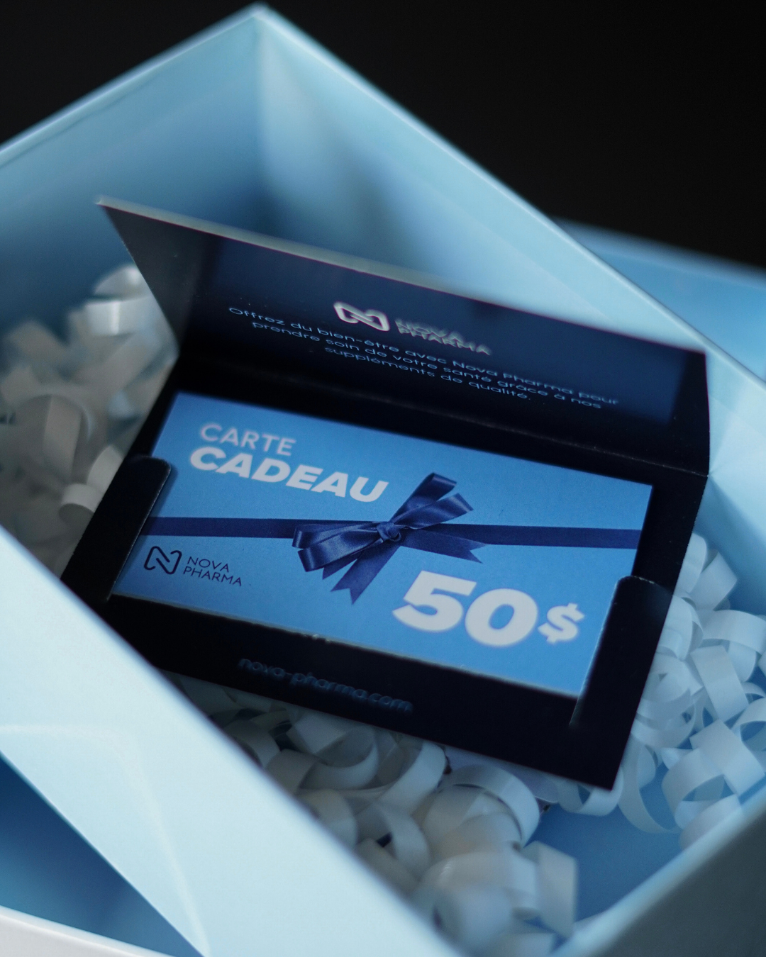 A 50$ gift card from Nova Pharma displayed inside an open light blue gift box filled with white crinkle paper.